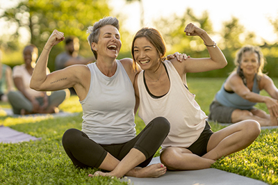 Two healthy women are sitting in the park with their hands raised